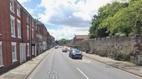 Vehicles travelling down Exeter Street, with red-brick houses along the side.