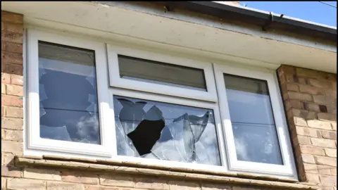 Hertfordshire Police A smashed white PVC window with four panes, in a red brick house.