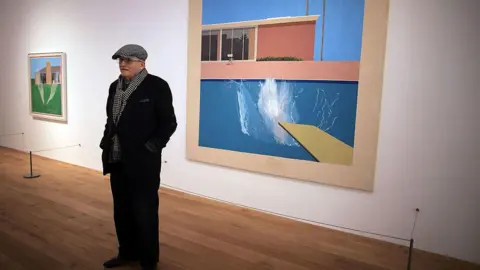 Christopher Furlong/Getty Images David Hockney stands in dark clothing in front of 'A bigger splash 1967', one of his most famous paintings