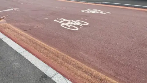 Red road with yellow lines faded out and two white bicycles painted on the road