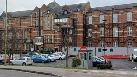 David Martin Royal Hampshire County Hospital, a large handsome brown-bricked Victorian building. A car park outside includes some portable cabins.