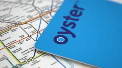 A blue Oyster card is lying over a map of the London Underground with the area around High Street Kensington in focus, with yellow and green circle lines shown on the map