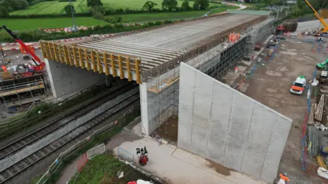 HS2 The Carol Green railway bridge shown during construction, it is a concrete structure flanked with scaffolding, cranes and other construction equipment can be seen either side