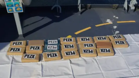 National Crime Agency A selection of 19 brown packages laid pout on a boat deck, measuring about 10in by 5in by 2in each and labelled 