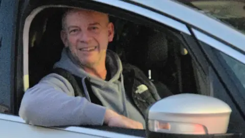 Paul Eve Paul Eve is wearing a grey hoodie and a black body warmer. He is smiling from behind the wheel of his silver taxi, with one arm leaning out the window.