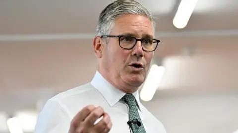 PA Media Sir Keir Starmer, in a white shirt and black rimmed glasses, speaks to ship builders during his visit to BAE Scotstoun shipyard in Glasgow