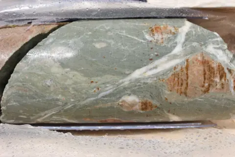 British Geological Survey A close up of a marble effected green rock with shades of orange