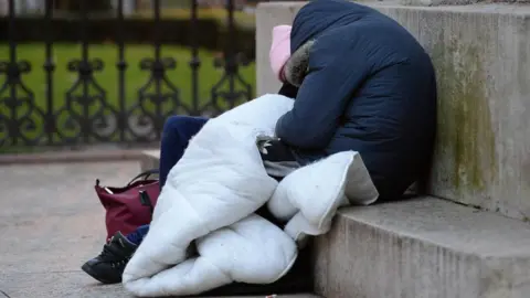 A homeless woman in a navy coat sleeping on concrete steps.