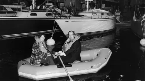 Getty Images A black and white photo of Maralyn and Maurice Bailey on a life raft. 