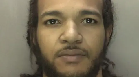 Mugshot of Rhemeese Lawrence-Hayden against a beige backdrop. he has a expressionless face and looking straight into the camera