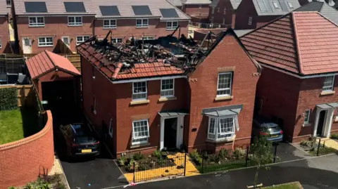 A new build property which has no roof after it was gutted by fire. Fallen beams and charred remains can be seen from an aerial view of the property.