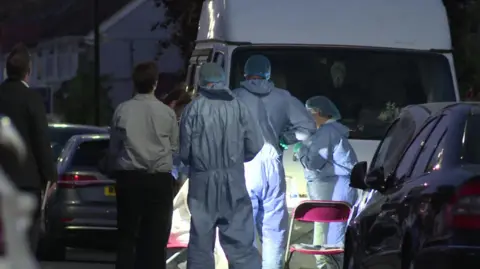 People in blue forensic suits working in torchlight on the street by a white van