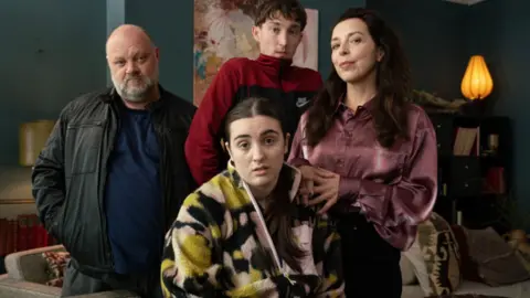 Four adults look at the camera, three look very serious while one woman is smiling