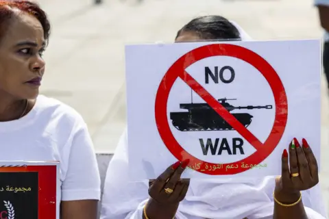 SALVATORE DI NOLFI/EPA A woman holds up a sign saying 'no war'. It shows an image of a tank under a red stop sign.