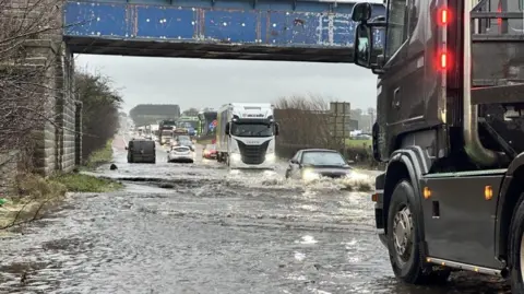 Lorries and vehicles travelling through flooded water on a road between Moira and Ballinderry.