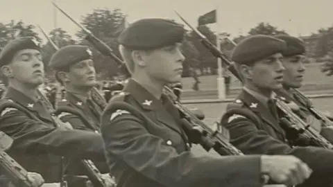 Angela Bushby A black and white image showing young members of The Parachute Regiment marching on a parade square. The soldiers are carrying SA80 rifles with bayonets fixed.
