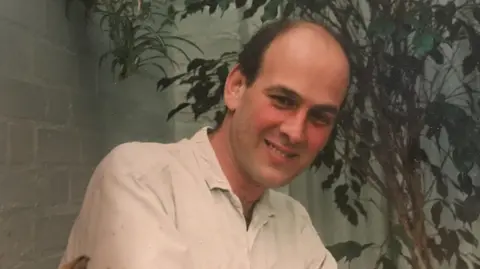 Cathy Johns An old photo of Michael, who is wearing a white shirt and smiling at the camera.