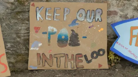 A close up of a homemade painted placard that reads "keep our poo in the loo"