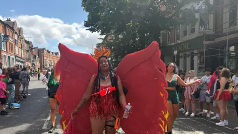 A woman wearing a red outfit which has wings in front of other people in a parade