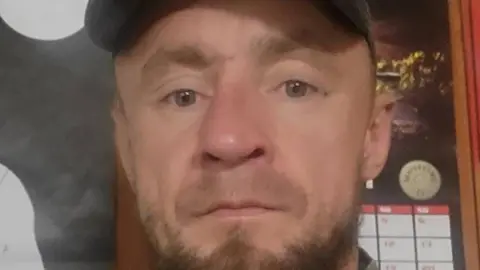 Piotr Pruszak has a light brown beard and wears a cap.