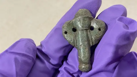 A hand wearing a purple glove, holding a small medieval metal dagger tip