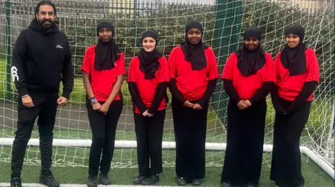 City Academy Bristol Five school pupils in sports hijabs stand next to their male teacher inside a football net