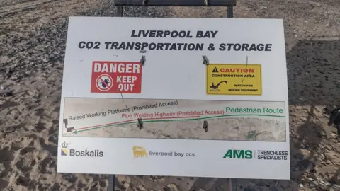 Linda Millwall The image shows a caution sign alerting visitors of a beach about works being done there. Behind the sign you can see the sandy beach.