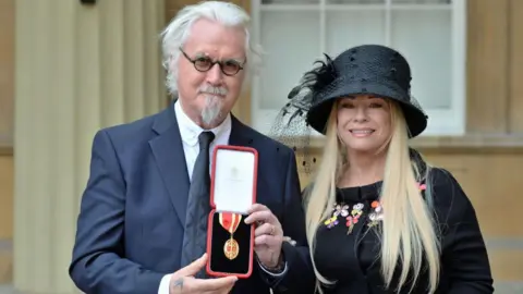 Glasgow to celebrate Sir Billy Connolly with weekend of events 5 Getty Images Billy Connolly showing his medal to the camera, after being knighted. He is standing outside Buckingham Palace with his wife Pamela Stephenson.