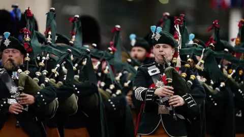 PA Media Members of the Royal Regiment of Scotland during a military procession for the 80th anniversary of VE Day - they are dressed in full regalia and playing the bagpipes as they march