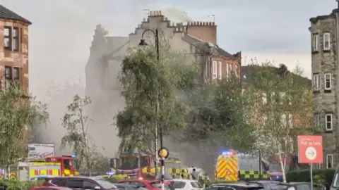 BBC A general view of the scene in Rutherglen. There are a number of emergency vehicles including fire engines and an ambulance and smoke.