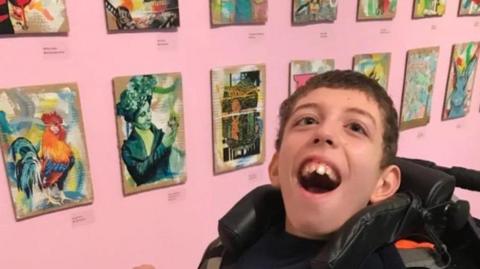 Noah smiling in front of some of his art