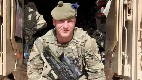 Nicholas Hart wearing army uniform and holding a gun