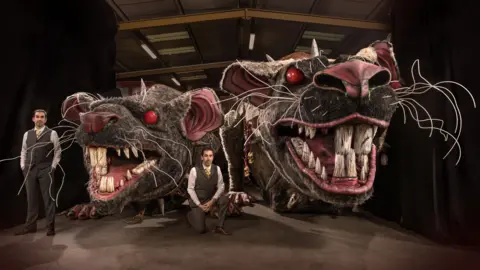 The Twins FX Paul and Gary stand next to two giant rat heads. The rats are baring their sharp teeth