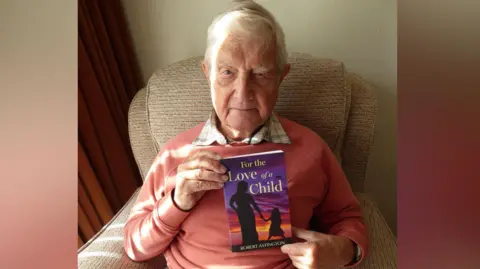 Robert Astington holds the book he has written, "For the Love of a Child"