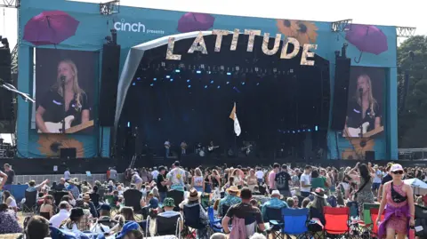 Getty Images Billie Marten, who has blonde hair and is wearing a black top, performs on a large blue stage during Latitude 2022. There is a busy crowd watching on.