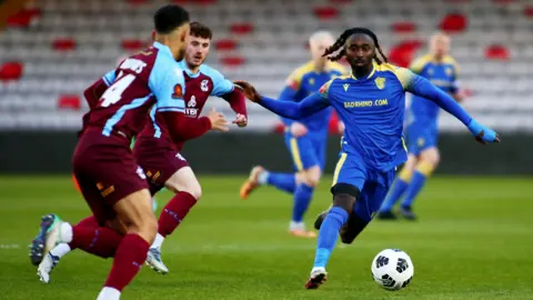 A photo from the 2024 County Senior Cup Final between Scunthorpe United and Spalding United. It shows two Scunthorpe United players running towards a Spalding United player who has the ball. 