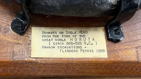 Close-up of a label on the head's wooden mount, giving some details of where it was found