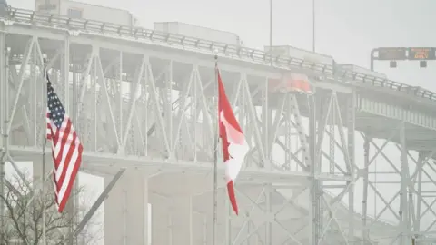 The Blue Water Bridge at the border crossing with the US at Sarnia, Ontario. US and Canada flags are in the foreground. 