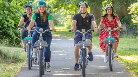 Four people wearing cycling helmets ride bikes along the path in the above picture.