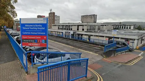 Google External view of the entrance and sign which reads 'Burnley General Teaching Hospital' showing vehicle parked outside the main building