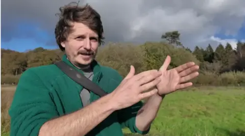 Person stood in front of green field with a green fleece jumper on