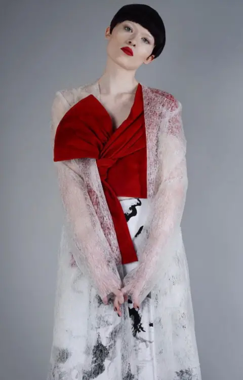 Nadia Pinkney A model wearing a red top with knots in the material, a black and white skirt and a sheer jacket.