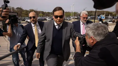 Bloomberg via Getty Images George Santos walking in front of his posse as press cameras take pictures of him