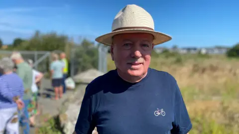 A man wearing a navy Tshirt and a beige straw hat.