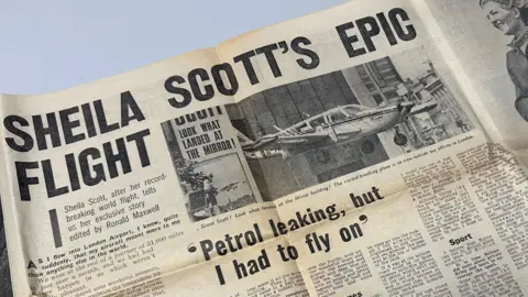 David Turner A page from an old newspaper with the headline "SHEILA SCOTT'S EPIC FLIGHT". The article includes a picture of a small plane. A sub-headline reads: "Petrol leaking, but I had to fly on".