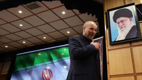 محمدبکر قالیباف، رئیس مجلس شورای اسلامی پس از سخنرانی در یک کنفرانس مطبوعاتی در تهران (3 ژوئن 2024) از مقابل عکسی از آیت الله علی خامنه ای رهبر معظم انقلاب عبور می کند.