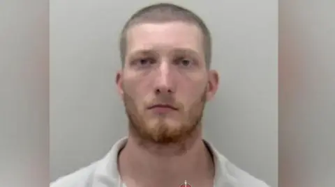 Young man with short cropped hair and a ginger beard looking to camera.