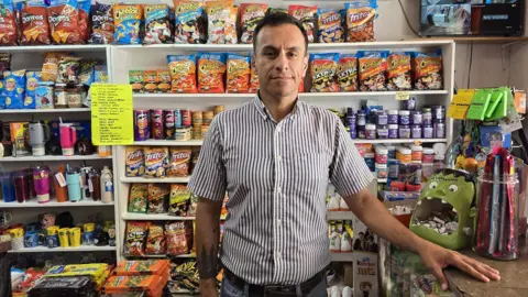 Mexican shop owner Adrian Ramos  looks at the camera