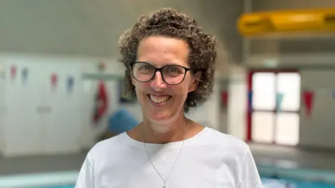 A woman with curly hair, wearing a white t shirt and necklace.