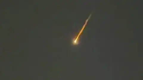 Alfie Chenery A stream of orange light and smoke in the black night sky.